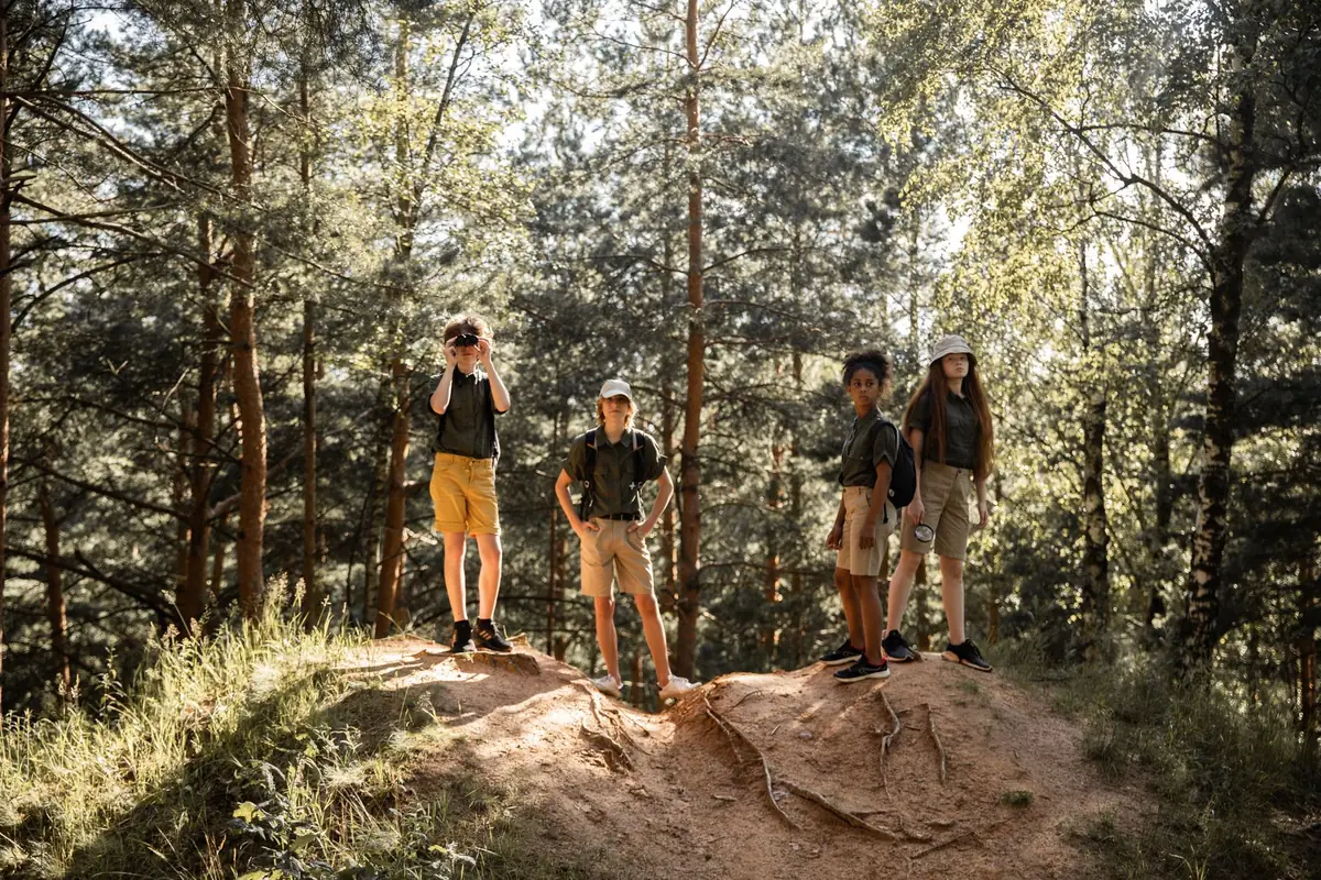 A group of children hiking along a forest trail among tall pine trees