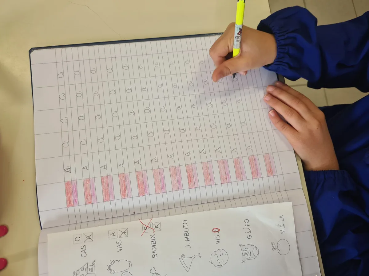 A child's hand writing letters in a notebook with a yellow highlighter nearby