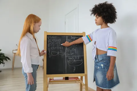 A girl working out a math problem on a chalkboard easel in a bright classroom