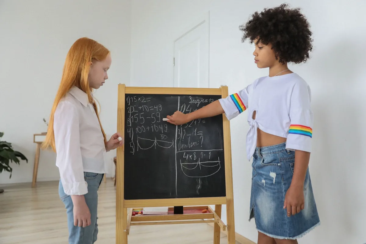 A girl working out a math problem on a chalkboard easel in a bright classroom