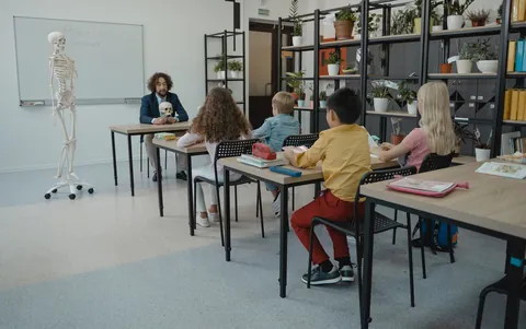 Elementary students seated at desks in a science classroom with a skeleton model