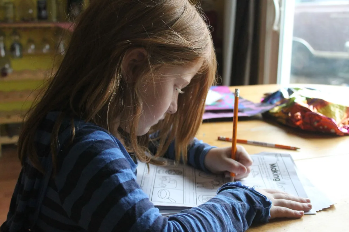 A child concentrating while writing in a workbook with a pencil