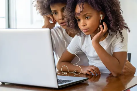 Two children using a laptop together at a table while learning