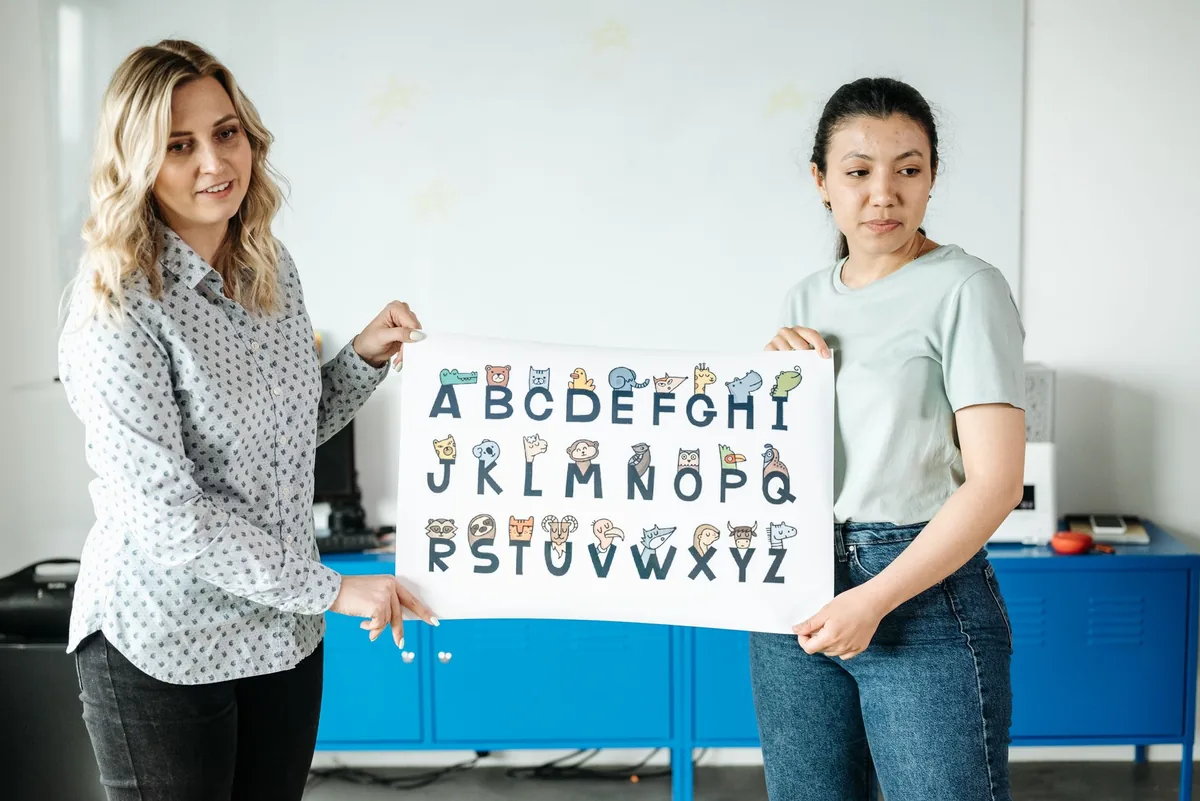 Two adults holding up a large card showing the full alphabet in a classroom