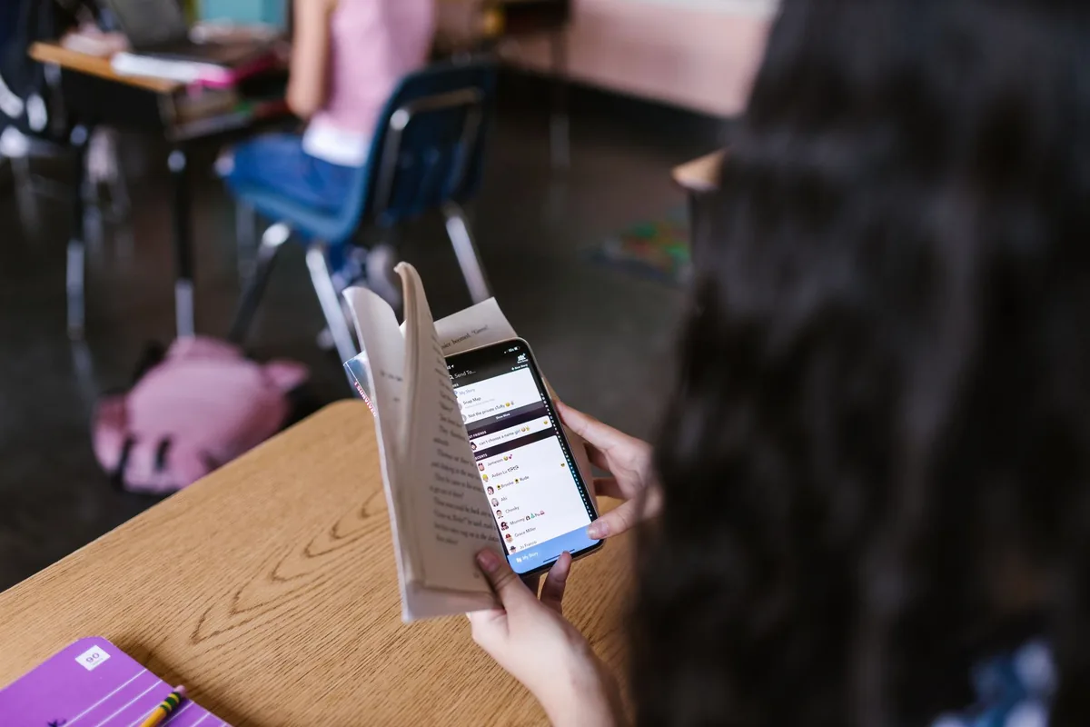A student holding a smartphone over a desk in class