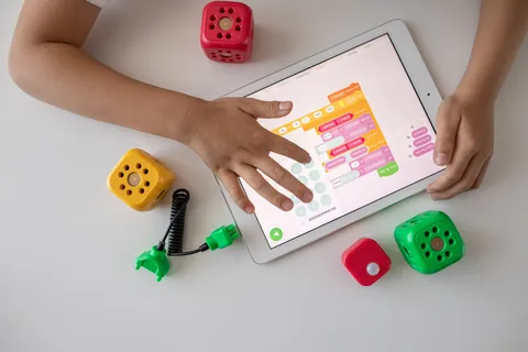 A child's hands using a coding app on a tablet with colorful blocks